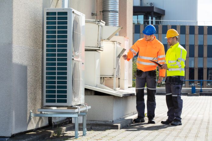 Two HVAC technicians inspecting a rooftop air conditioner unit on a commercial building.