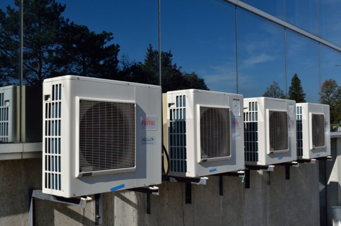 An image of a heat pump system, with a sleek and modern design, mounted on a wall. The unit has a digital display and is surrounded by greenery, indicating its environmentally friendly benefits.